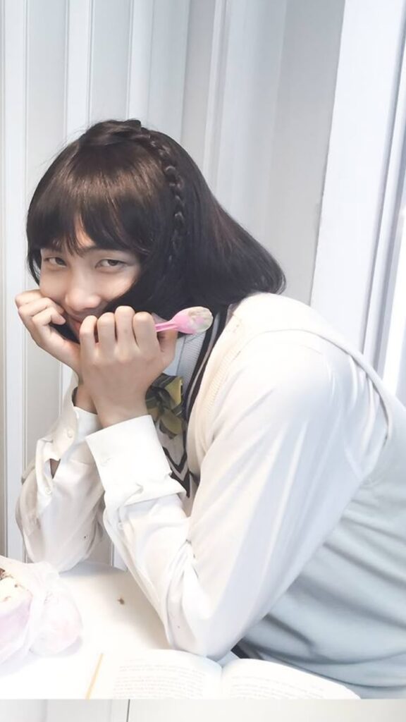 A man with long black hair in a white shirt, playfully embodying a BTS member's style.RM