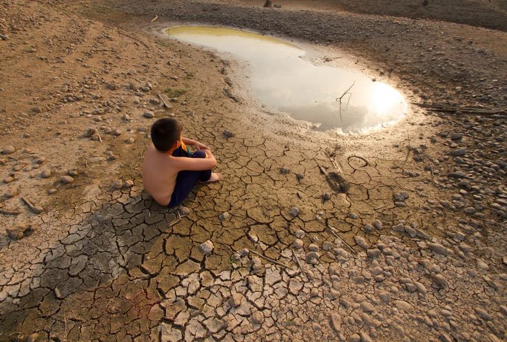 A child rests on the ground near a water hole, highlighting the urgent water crisis in Pakistan under ominous clouds.